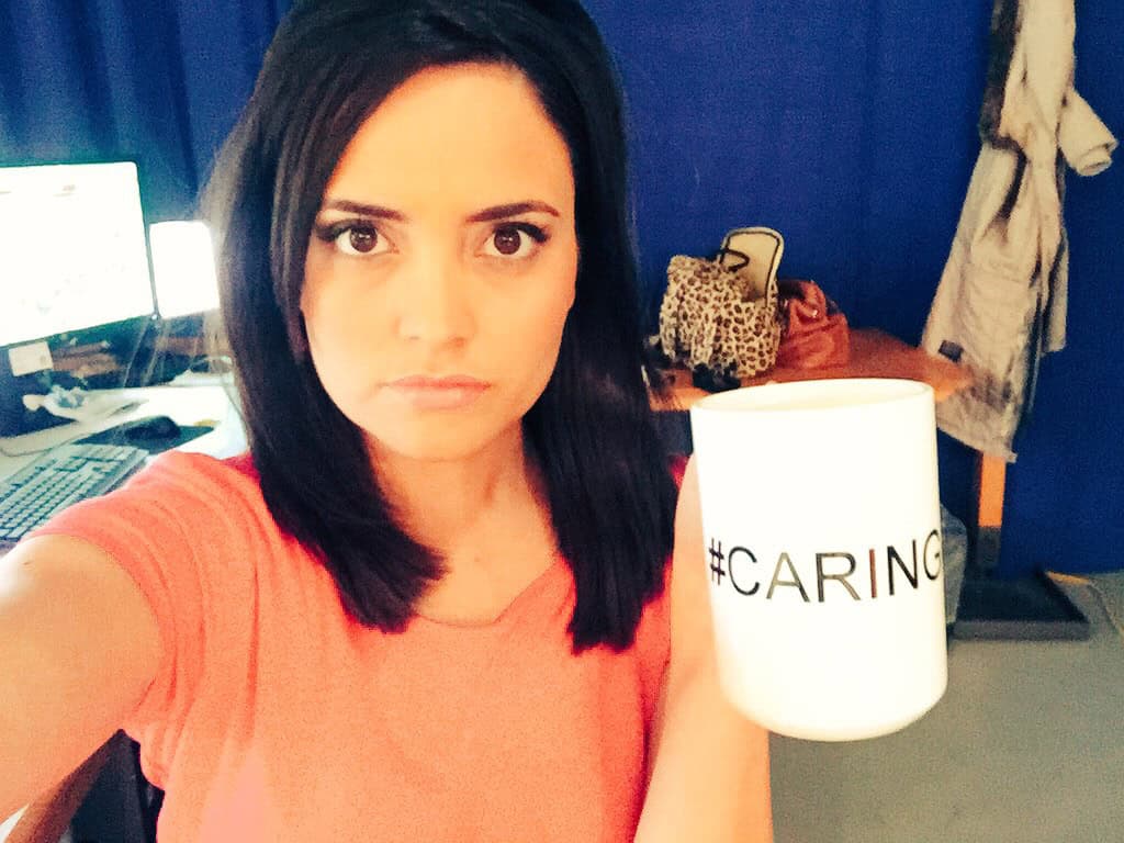 Woman with short black hair holding a mug that says #CARING