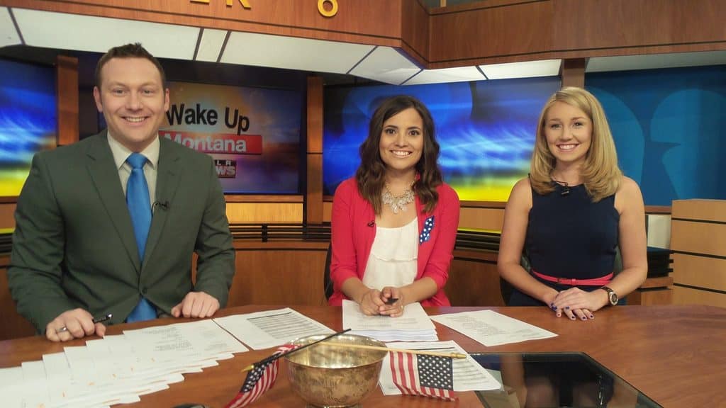 Three news anchors sitting and smiling at a news desk